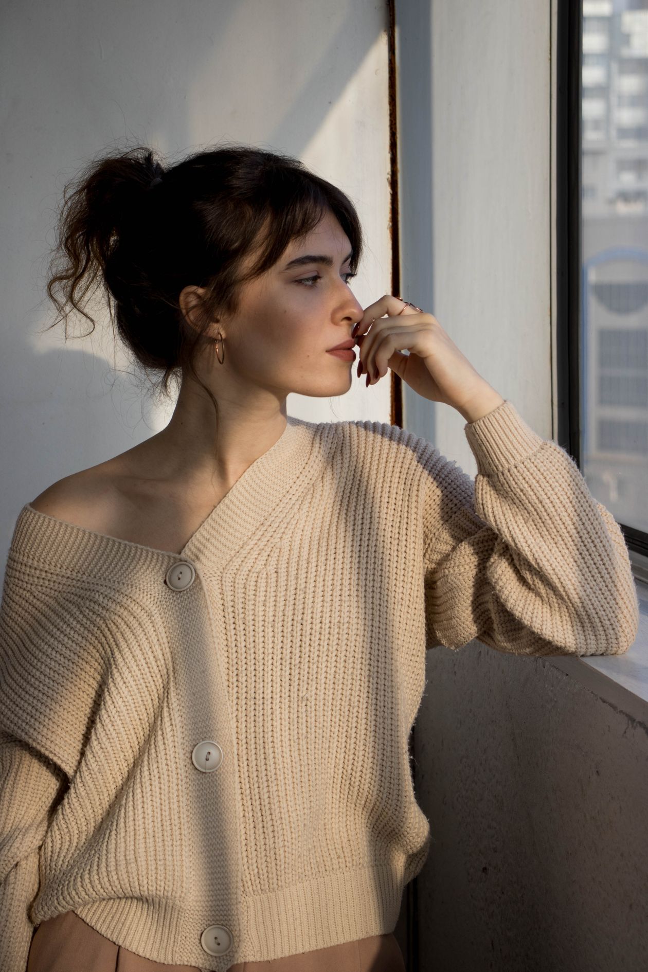 Femme en pull chaud regardant par la fenêtre, illustrant le fait de s'habiller chaudement plutôt que de monter le chauffage
